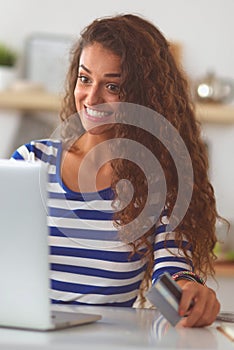 Smiling woman online shopping using computer and credit card in kitchen