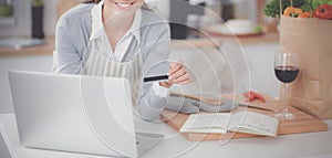 Smiling woman online shopping using computer and credit card in kitchen