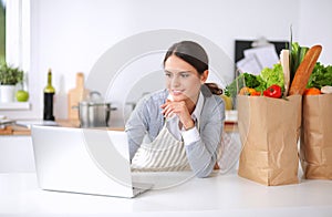 Smiling woman online shopping using computer and credit card in kitchen