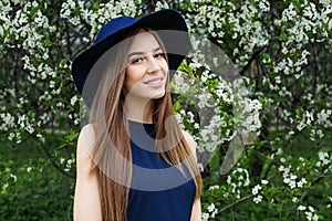 Perfect spring woman in blue hat outdoors. Smiling girl against flowers background