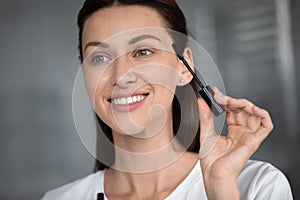 Smiling woman paint eyelashes with black mascara