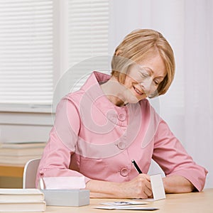 Smiling woman paying bills with checks at desk