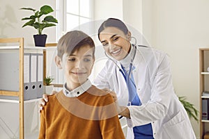 Smiling woman pediatrician examining preteen boy patient with stethoscope