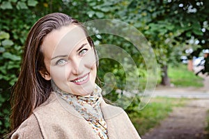 Smiling woman with a perfect smile, walking in the coat in autumn Park and looking at camera.