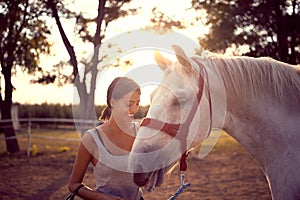 Smiling woman pets her white horse. fun on countryside,  golden hour. Freedom nature concept