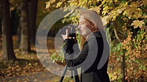 smiling woman photographer takes photos of landscape in autumn sun park