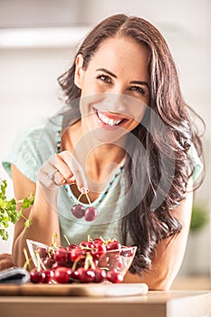 Smiling woman picks two cherries from a seethrough bowl indoors photo