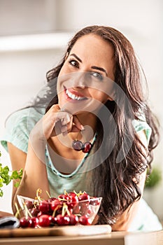 Smiling woman picks two cherries from a seethrough bowl indoors photo