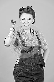 Smiling woman in pin-up style showing wrench in hand on camera. Caucasian brunette model posing in retro fashion and vintage