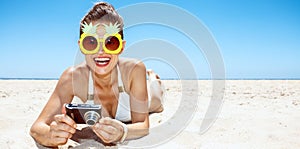 Smiling woman in pineapple glasses with photo camera at beach