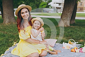 Smiling woman play and sit on green grass in park, rest and hug hold soap bubble blower with little cute child baby girl