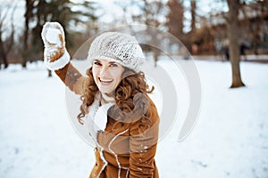 Smiling woman playing snowball outside in city park in winter