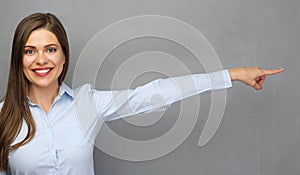 Smiling woman pointing finger to copy space on gray wall