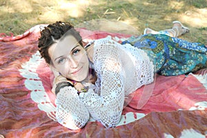 Smiling woman portrait rest outdoor lie on an indian tapestry in park, looking at camera