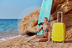 Smiling woman posing with suitcase and binoculars at sea beach. Future life and new horizons concept. New way idea