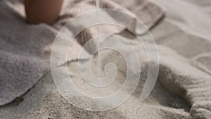 Smiling woman pouring sand between fingers lying on summer beach close up.