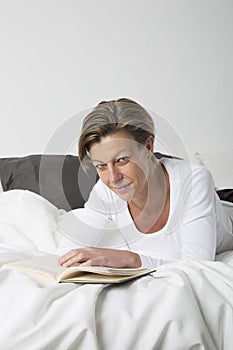 Smiling Woman reading a book in bed