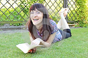 Smiling woman reading book on the grass in garden