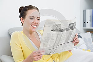 Smiling woman reading newspaper on sofa at home