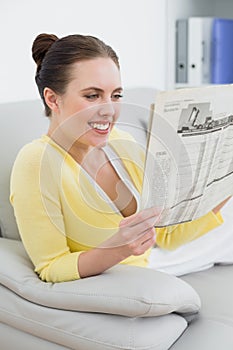 Smiling woman reading newspaper on sofa at home