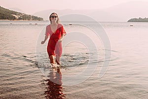 Smiling woman in red beach tunic running across the sea