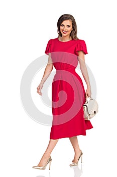 Smiling Woman In Red Dress, Gold High Heels And Beige Purse Is Walking