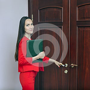 Smiling woman in a red suit with documents in hand knocking at the door