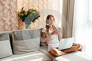 Woman with cup of tea watching movie on laptop at home photo