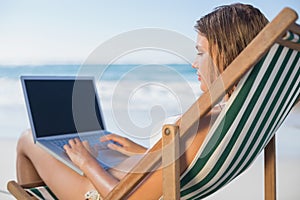 Smiling woman relaxing in deck chair on the beach using laptop