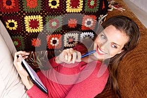 Smiling woman relaxing on sofa with pen and book