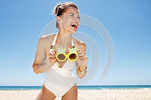 Smiling woman at sandy beach holding funky pineapple glasses