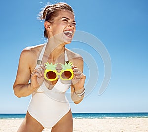 Smiling woman at sandy beach holding funky pineapple glasses