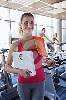 Smiling woman with scales and towel in gym