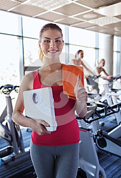 Smiling woman with scales and towel in gym