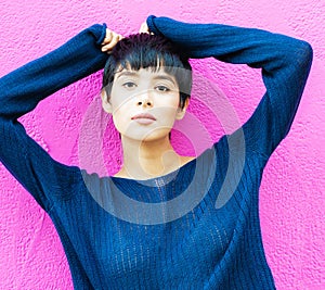 Smiling woman with short hair standing against pink wall.