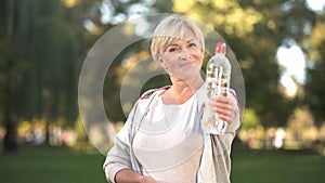 Smiling woman showing bottle of sparkling water before camera, healthy lifestyle