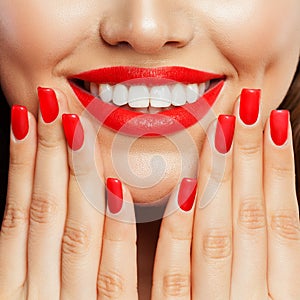 Smiling woman showing her hand with manicured nails. Red nail polish and makeup lips with bright red color tint lipstick
