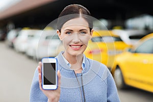 Smiling woman showing smartphone over taxi in city