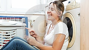 Beautiful smiling woman singing and listening music on floor at laundry room
