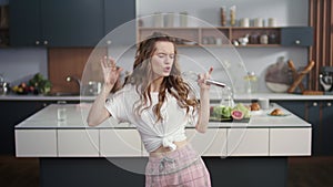 Smiling woman singing song in whisker in kitchen. Cheerful girl having fun