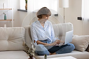 Smiling woman sit on sofa using laptop texting