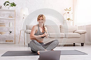 Smiling woman sits on mat in lotus pose and knits pigtail