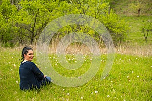 Smiling woman sits in spring grass