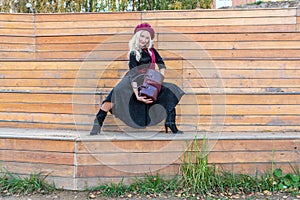 A smiling woman sits on a summer theater bench, made of wood in a burgundy coat and biret, an adult with tender lips, in