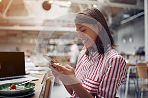 Smiling  woman sitting at cafe and texting on mobile phone