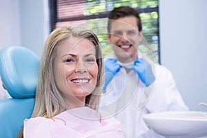 Smiling woman sitting on chair against dentist at medical clinic