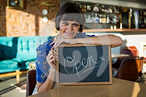 Smiling woman sitting in the coffee shop with a open sign