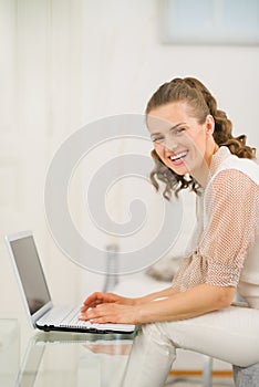 Smiling woman sitting on couch in living room and using laptop