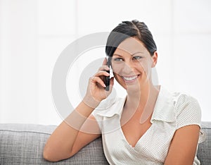 Smiling woman sitting on couch and talking mobile