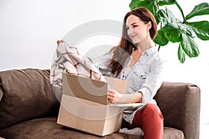 Smiling woman sitting on couch, unpacking carton, pleased with online order